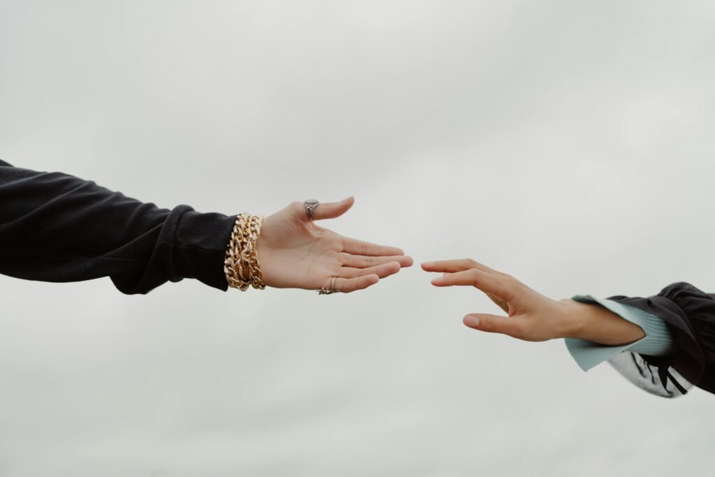 pexels photo 10667753 10667753 Close-up of two hands reaching for each other under a cloudy sky, symbolizing connection.