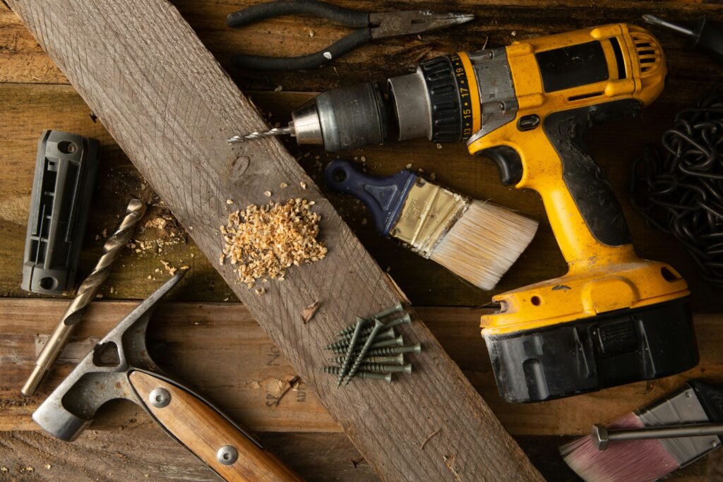 pexels photo 11398216 11398216 A close-up of various tools including a drill, hammer, and paintbrush on a wooden workbench.