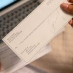 Individual holding a cheque over laptop, signifying online banking or financial transaction.