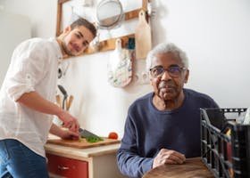 A young adult helping a senior in the kitchen, highlighting care and support at home.
