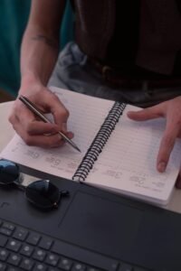 Young man writing in planner with sunglasses and laptop, capturing a stylish lifestyle in Buenos Aires.